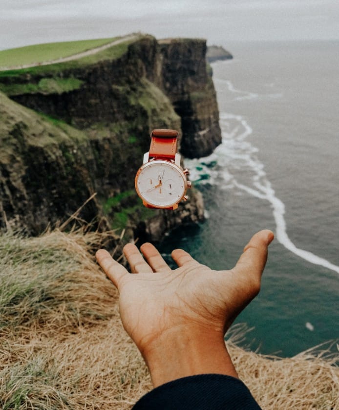 a hand and a wrist watch with the sea as background