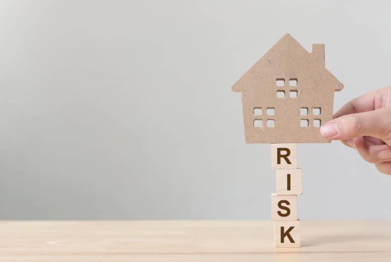 Hand holding a house on a wooden table with the word risk on wooden blocks